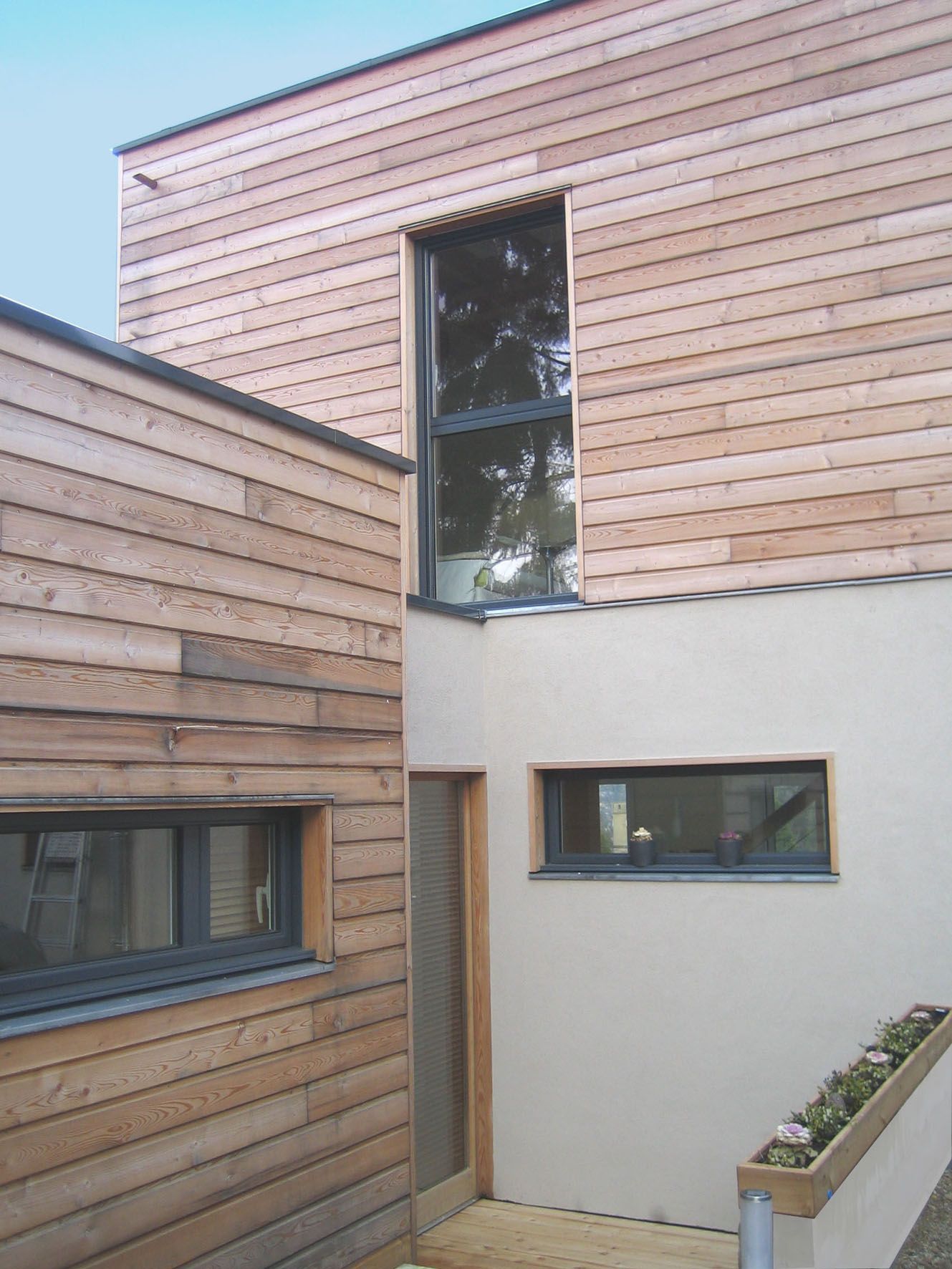 Vue extérieure d'un bâtiment moderne avec bardage en bois, fenêtres et murs en stuc clair.