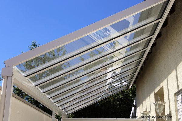 Modernes Glasvordach an der Hauswand, getragen von Metallstreben.