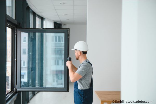 Handwerker kontrolliert geöffnetes Fenster in modernem Gebäude.