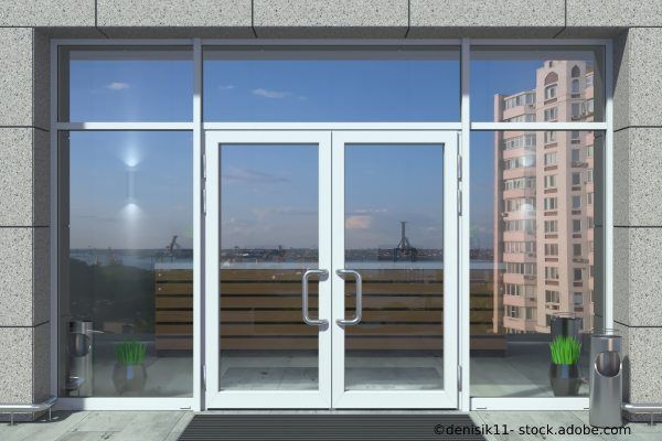 Doppelflügelige Glastür in Betonfassade mit Ausblick auf Stadt.