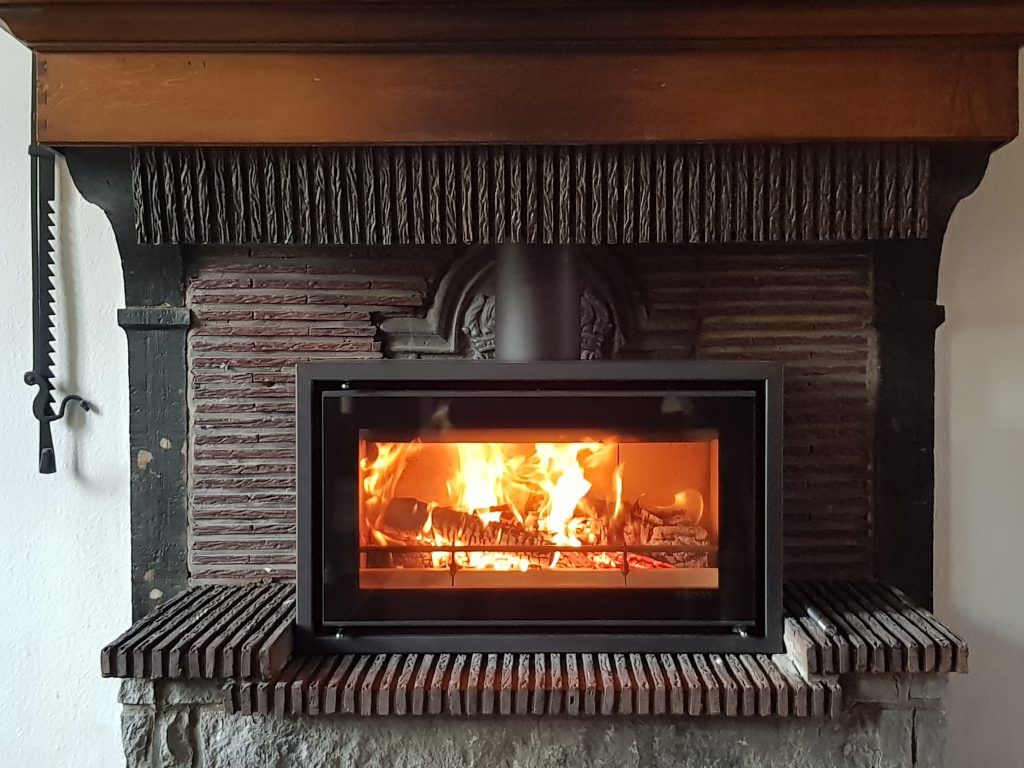 Poêle à bois aménagé dans une ancienne cheminée de brique noircie