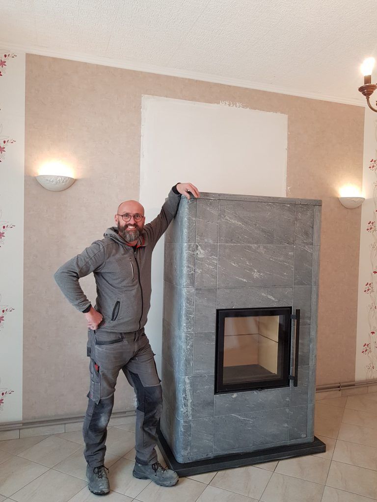 Poêle à bois en pierre ollaire Mammutti de Tulikivi avec employé qui pose à côté
