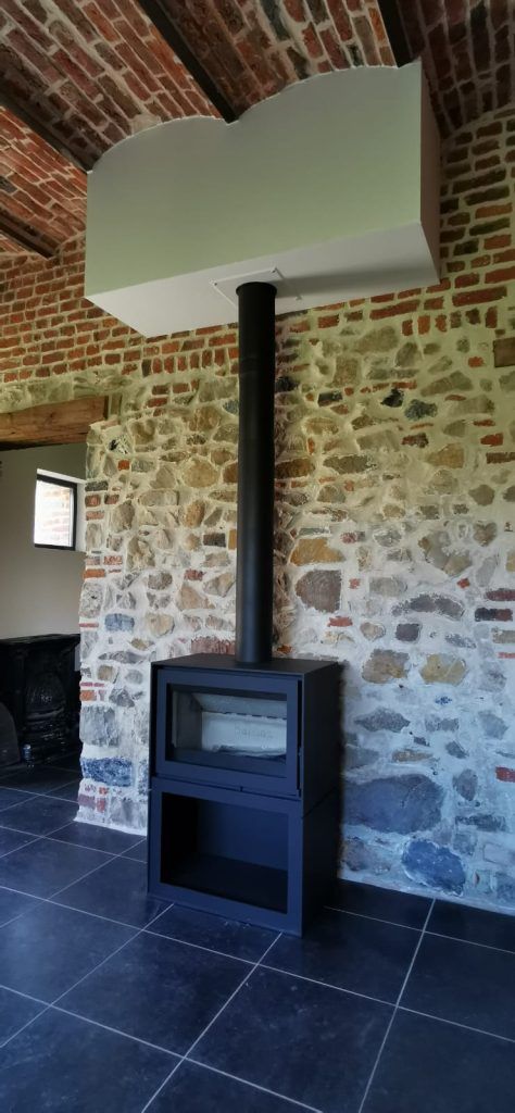 Poêle à bois carré noir avec mur en pierre apparente derrière