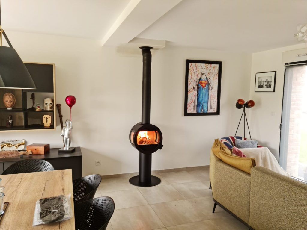 Poêle à bois de forme ronde devant mur blanc avec tableau et fauteuil sur le coté