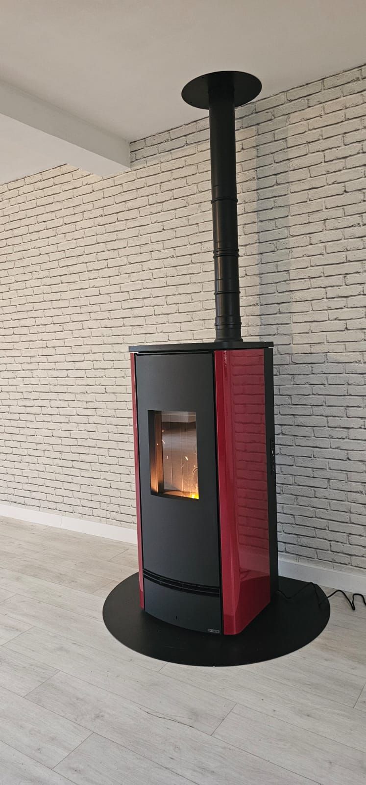 Poêle à pellets gris foncé et rouge disposé contre un mur de briques