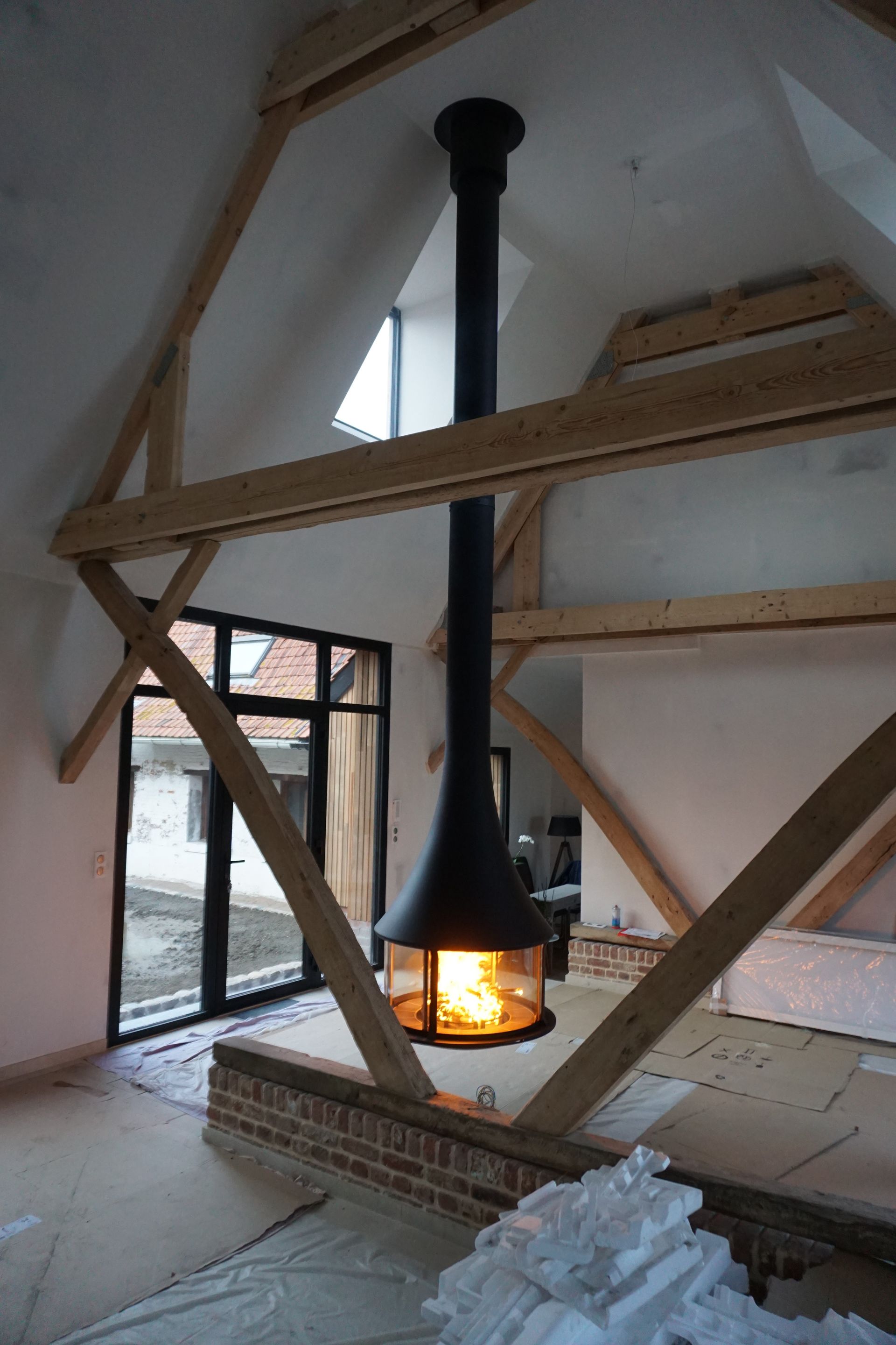 Cheminée design suspendue entre des charpentes