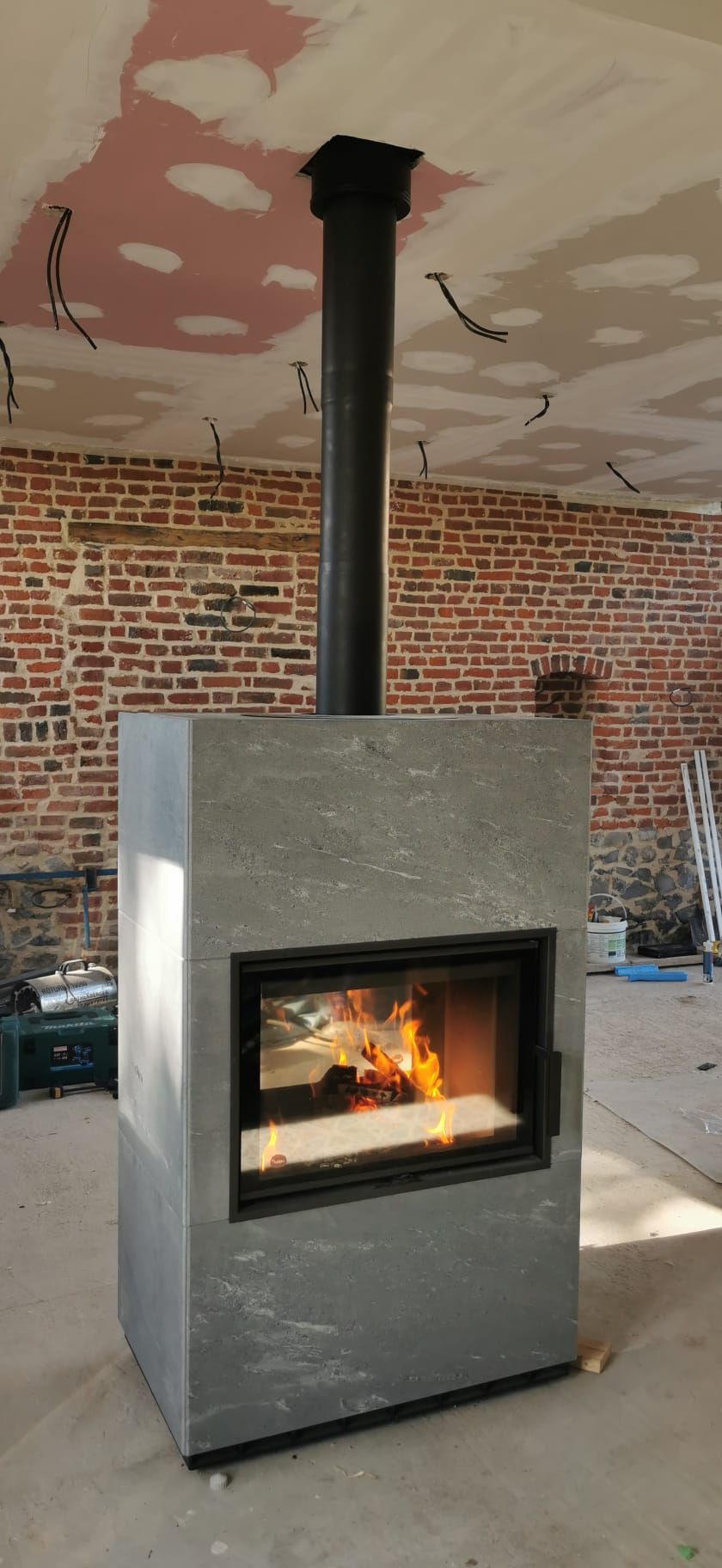 Poêle à bois gris de forme rectangulaire gris et réserve de bois sur le côtés gris de forme rectangulaire gris avec mur en brique derrière