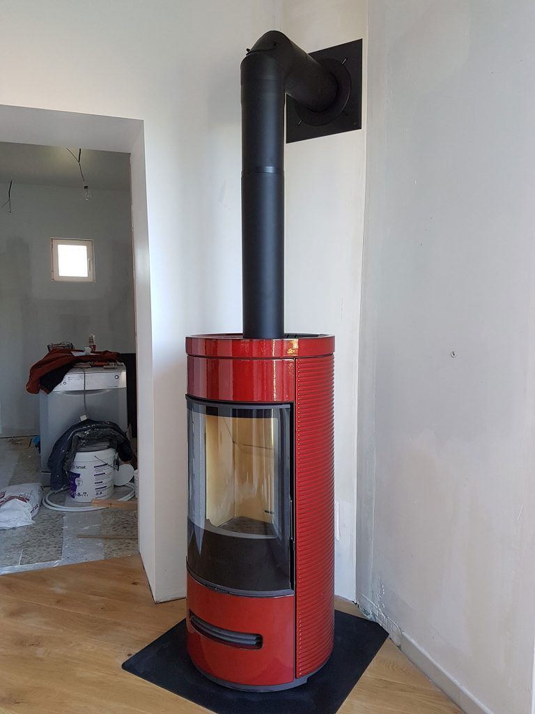 Poêle à bois de forme arrondi de couleur rouge contre un mur en coin