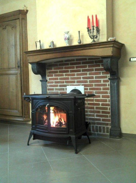 Poêle à bois de forme carré aménagé devant un ancien espace de foyer de cheminée en brique