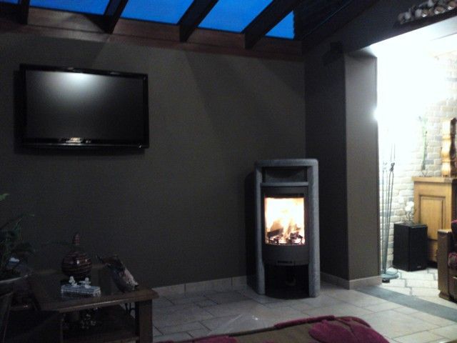 Poêle à bois dans le coin du salon avec télé accrochée sur le mur