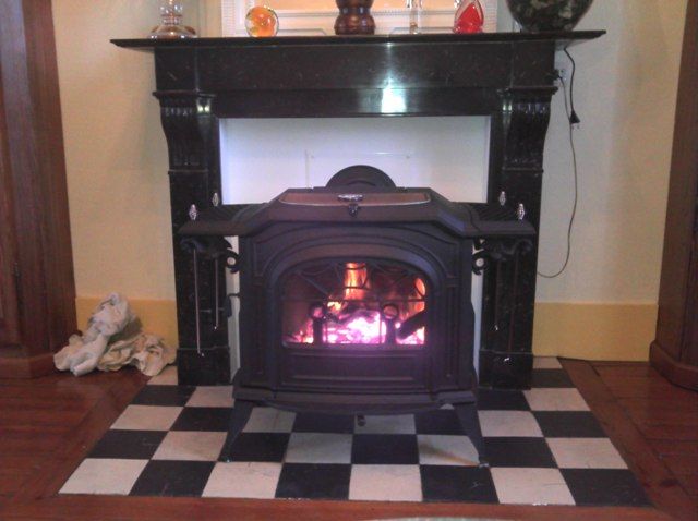 Poêle à bois de forme carré aménagé devant un ancien espace de foyer de cheminée avec du marbre noir en habillage