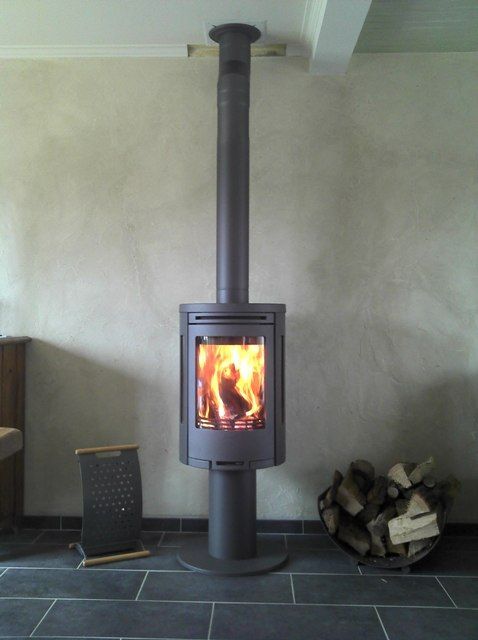 Poêle à bois de forme arrondi de couleur grise contre un mur