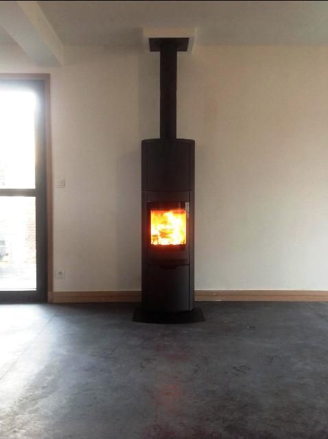 Poêle à bois de forme arrondi de couleur noir contre un mur et sol gris