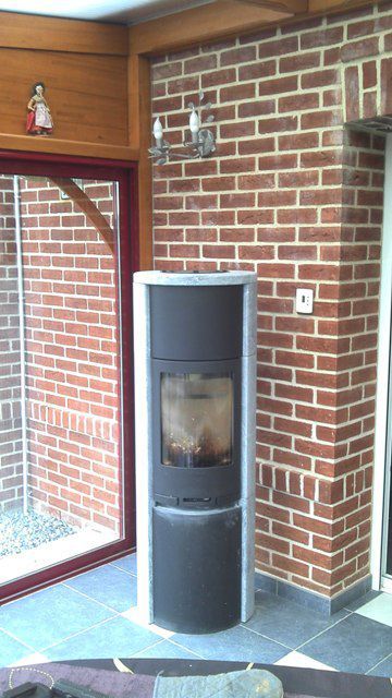 Poêle à bois de forme arrondi de couleur noir et blanche avec mur en brique derriére