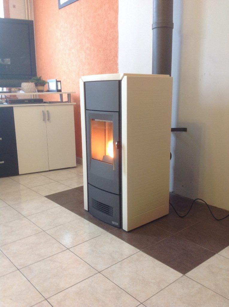 Poêle à pellets de couleur beige avec foyer allumé posé sur une plaque pour protéger le carrelage