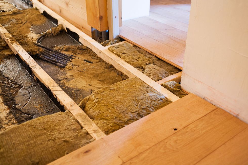 Sol en rénovation avec solives apparentes, saleté et parquet partiellement installé près d'une porte.