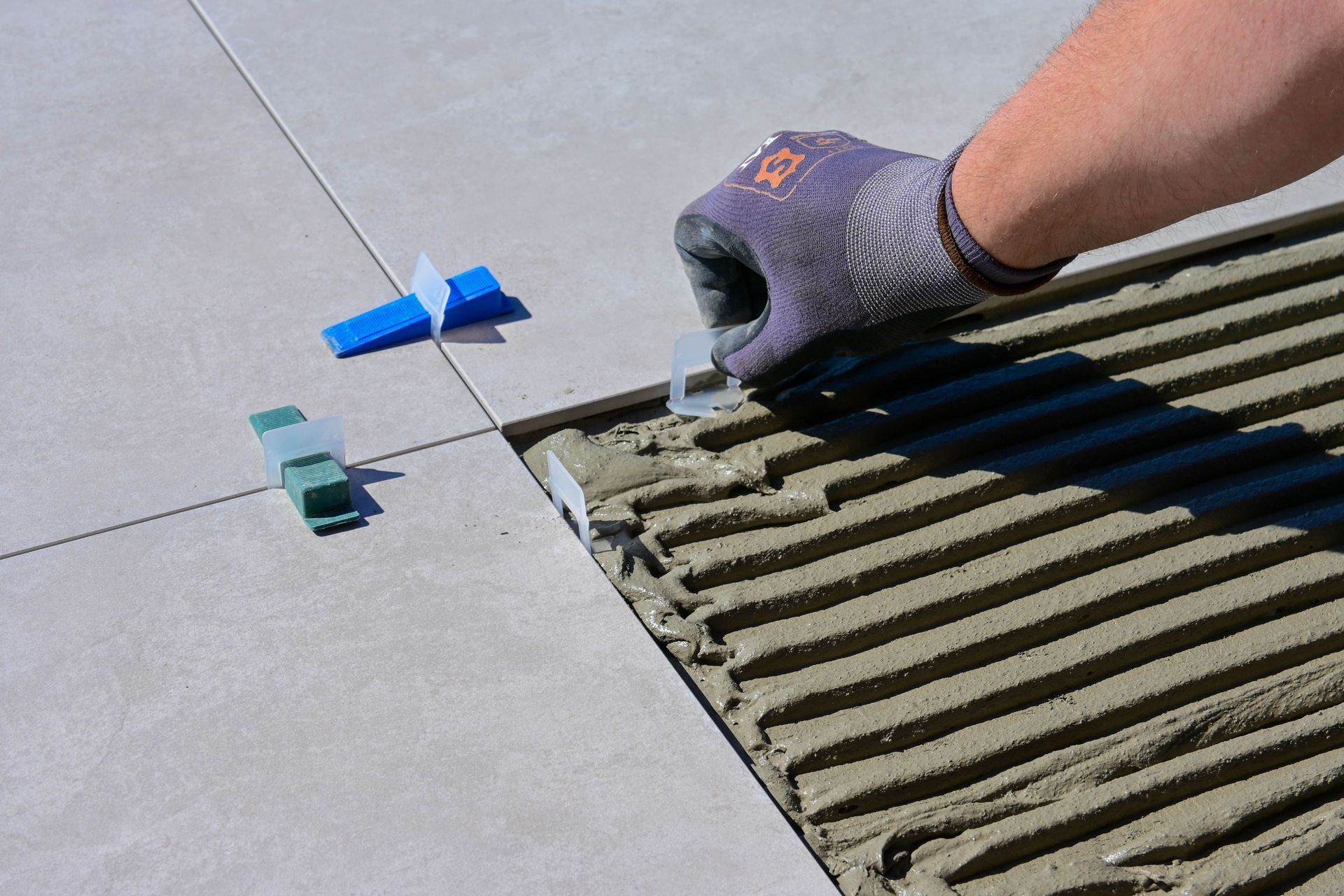 Main gantée étalant du mortier à côté d'entretoises de carreaux bleus sur un sol carrelé