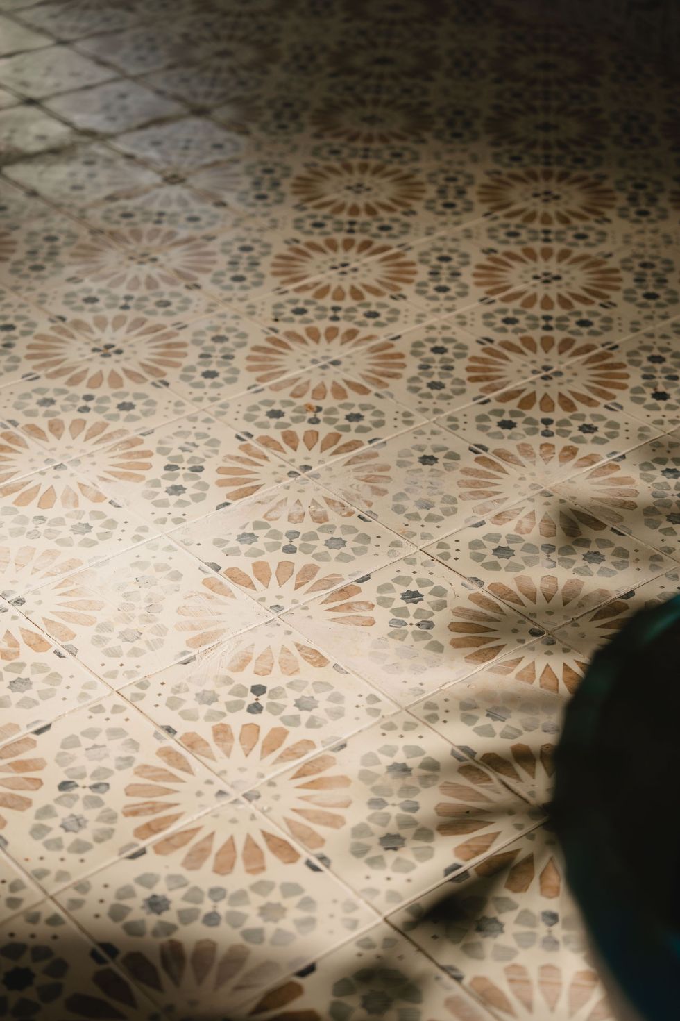 Sol carrelé à motifs floraux beiges et bruns, partiellement ombragé par le pied d'une personne en bas à droite