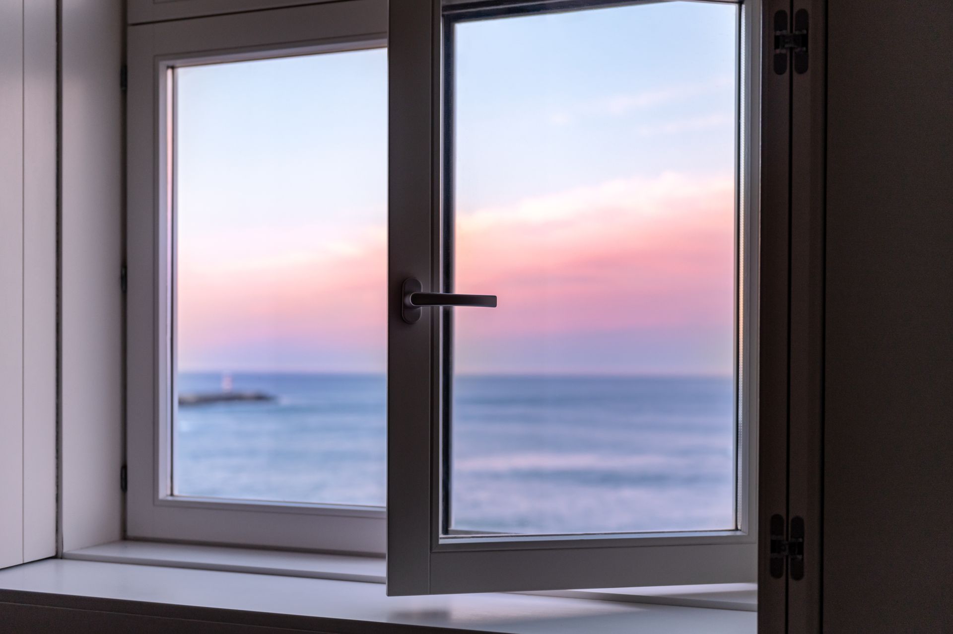 Una ventana abierta con vista al océano al atardecer.