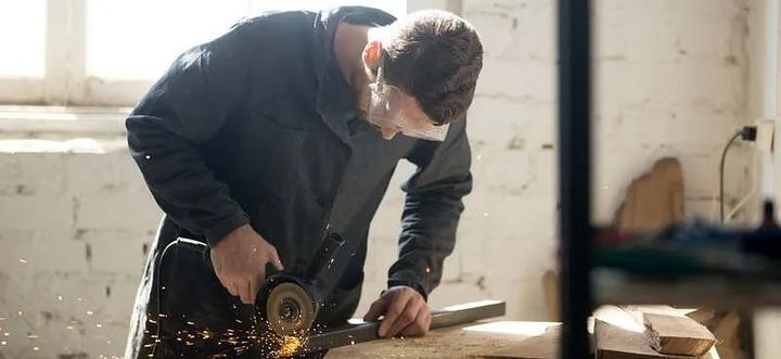 Un hombre está moliendo un trozo de metal con una amoladora en un taller.