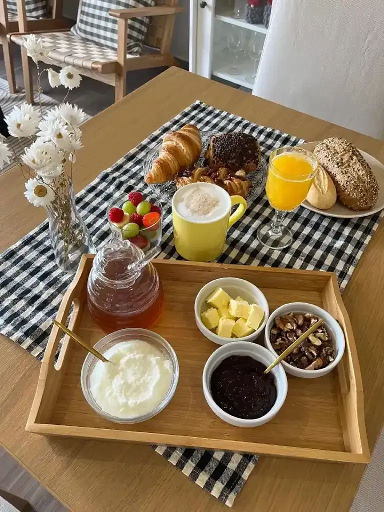 Desayuno: bandeja con yogur, mermelada, mantequilla, frutos secos, miel, croissant, café, zumo, uvas