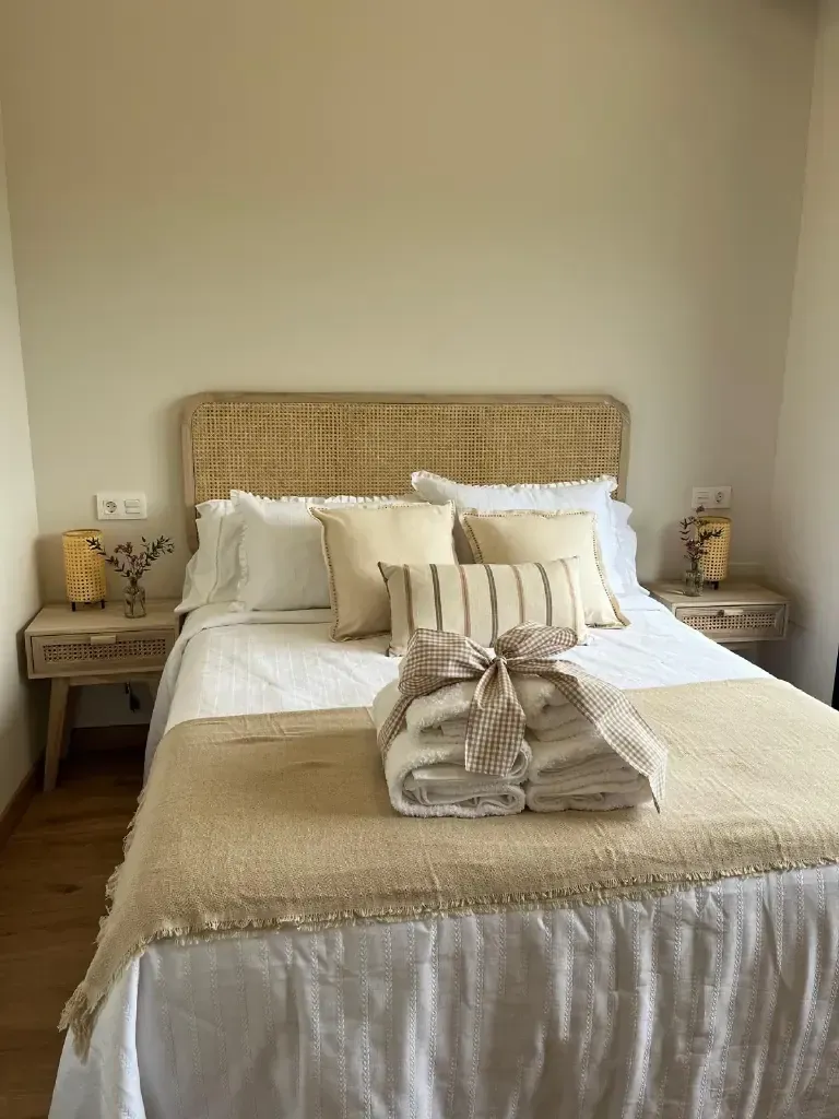 Dormitorio con cama, mesitas de noche y decoración. La cama tiene un cabecero color canela