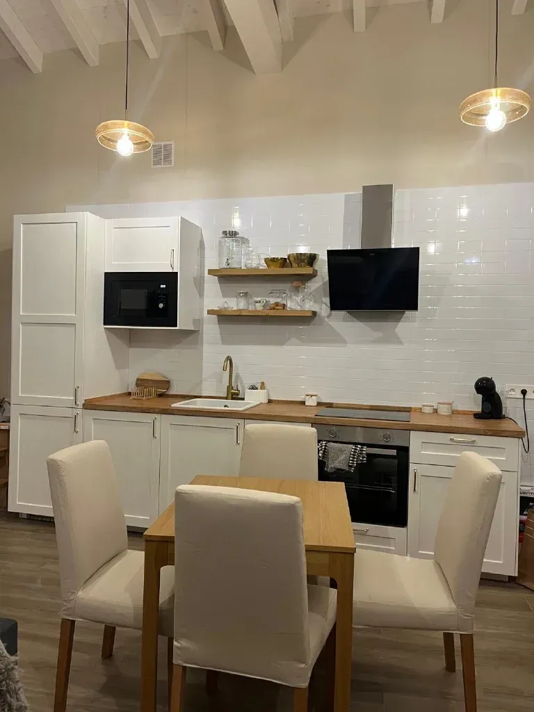 Cocina blanca con encimeras de madera, electrodomésticos negros y una mesa de comedor con sillas.