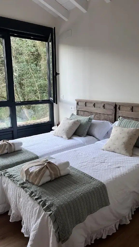 Dos camas individuales con ropa de cama blanca, mantas verdes y almohadas decorativas cerca de una ventana.