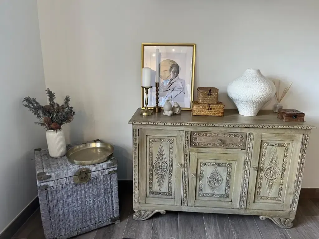 Un mueble vintage con decoración en un rincón. Incluye obras de arte, jarrones y cajas en tonos neutros.