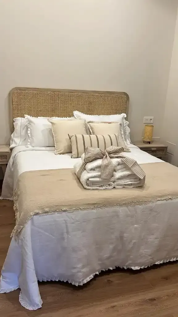 Dormitorio con cama, cabecero beige, ropa de cama blanca y beige, mesitas de noche y lámpara.