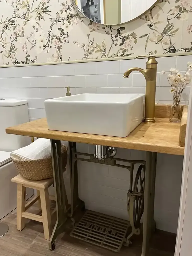 Baño con lavabo cuadrado blanco sobre mesa de madera, realizada a partir de una base de máquina de coser Singer.
