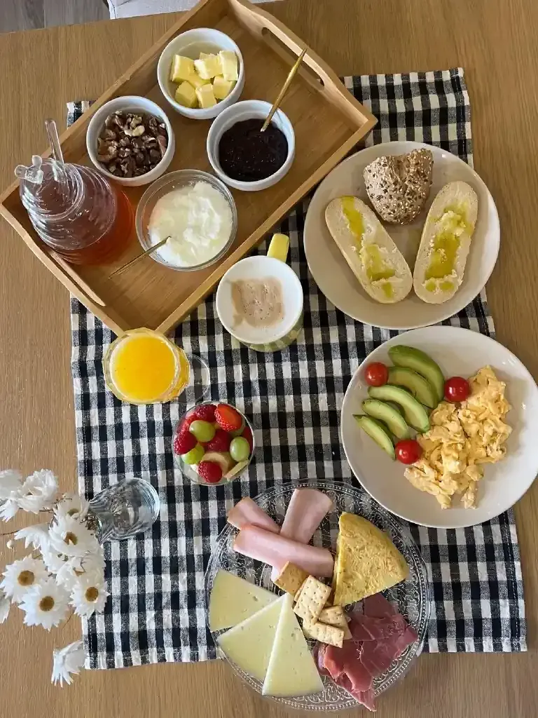 Desayuno compuesto por diversos alimentos: huevos, fruta, queso, yogur y pan.