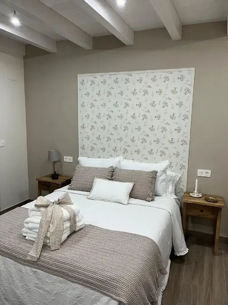Dormitorio con cama, mesitas de noche y cabecero floral. Predominan los tonos beige y blanco.