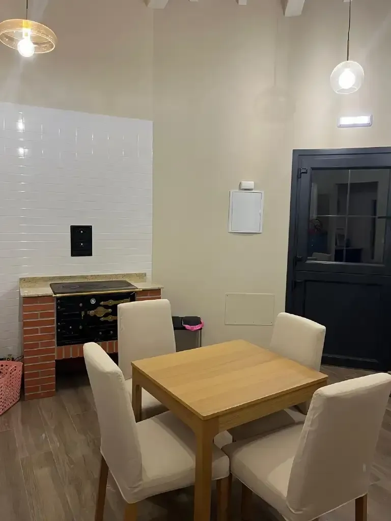 Un comedor con una mesa de madera, cuatro sillas, una estufa de ladrillo y una puerta negra.