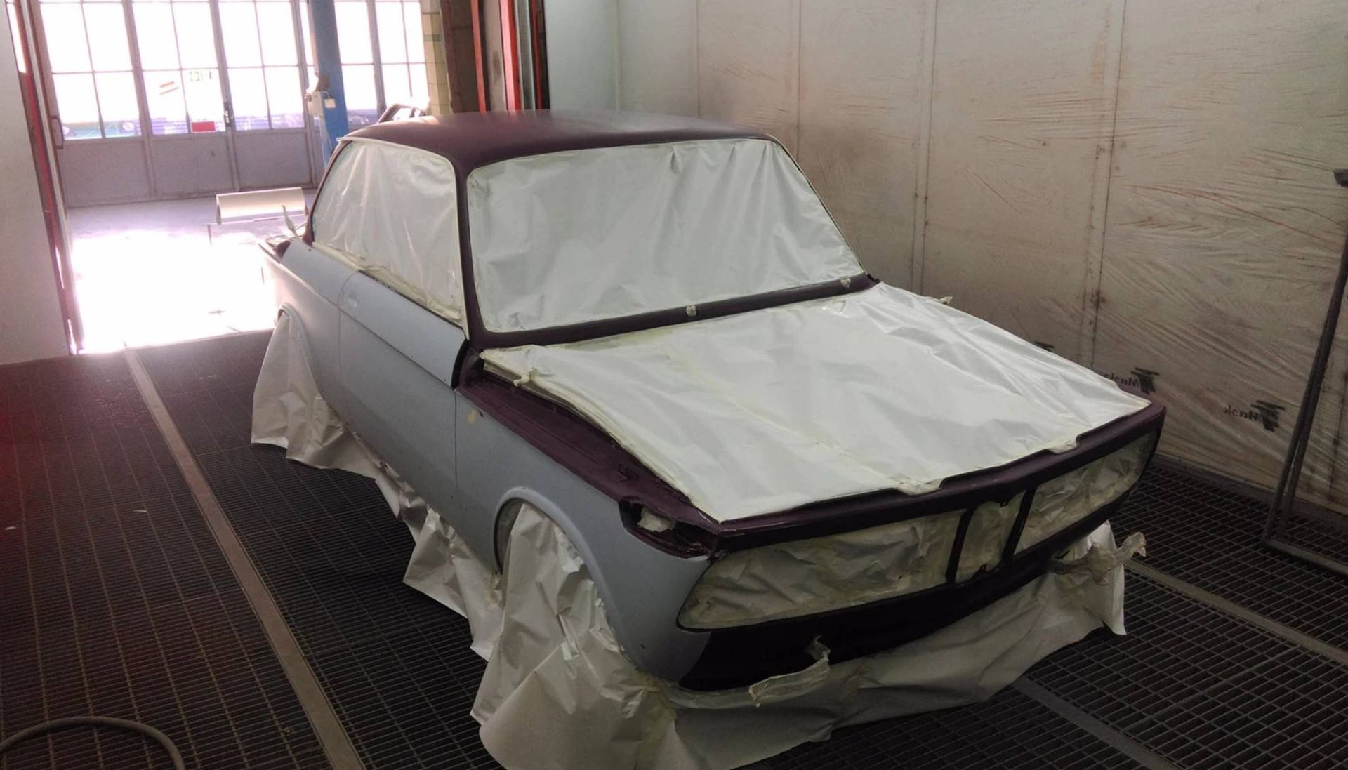 Un'auto d'epoca viene verniciata in una cabina di verniciatura; alcune parti sono ricoperte di carta bianca.