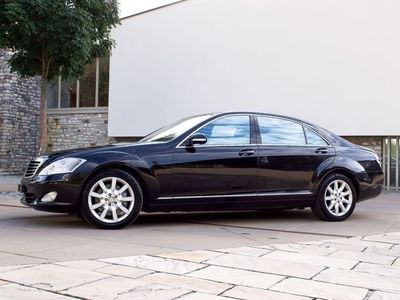 Eine schwarze Limousine parkte im Freien neben einer Steinmauer und einem weissen Gebäude.