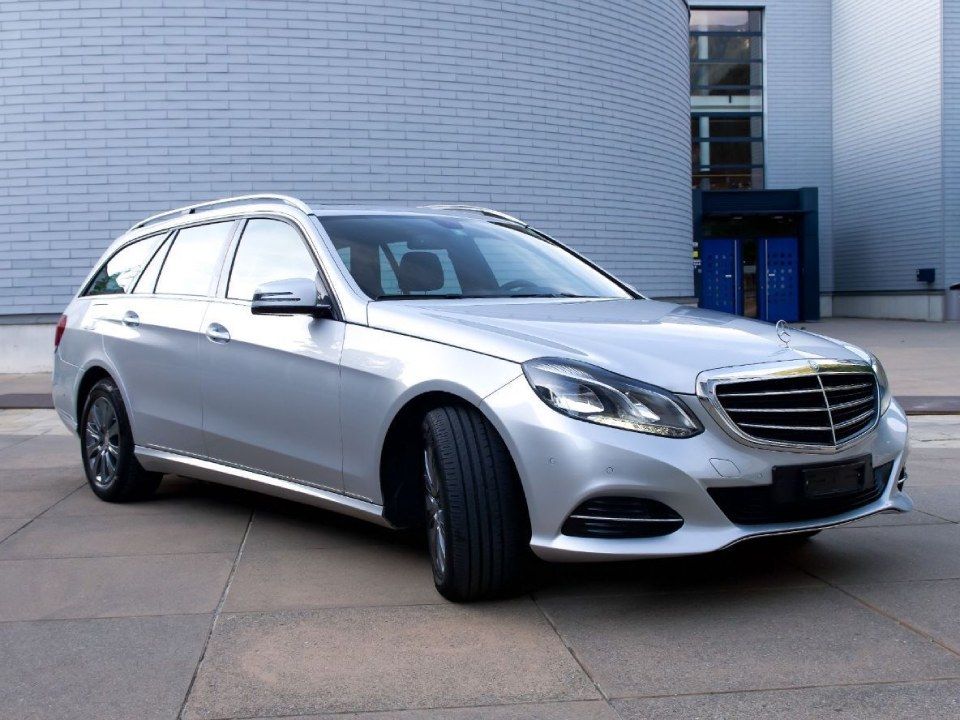 Eine silberne Mercedes-Benz Limousine parkt neben einem weissen Backsteingebäude.