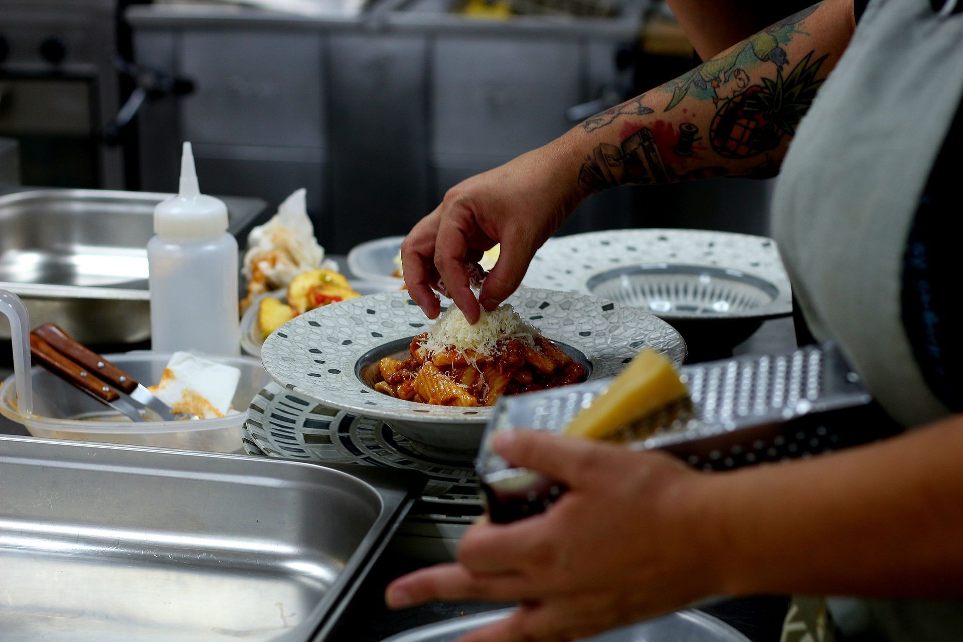 Chef rallando queso sobre un plato de pasta en la cocina de un restaurante.