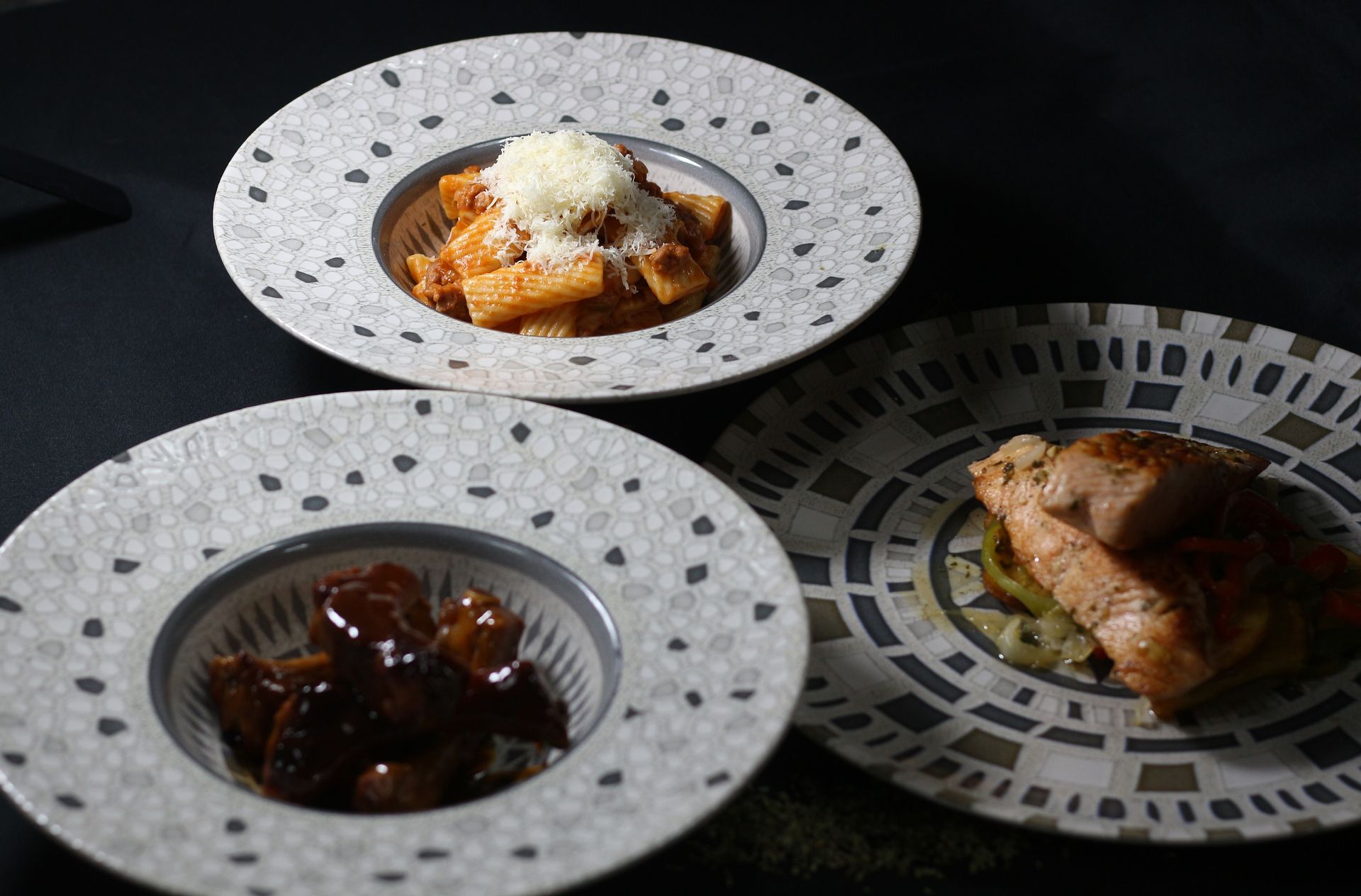 Tres platos de comida en platos decorativos: pasta, carne y un plato de pollo.