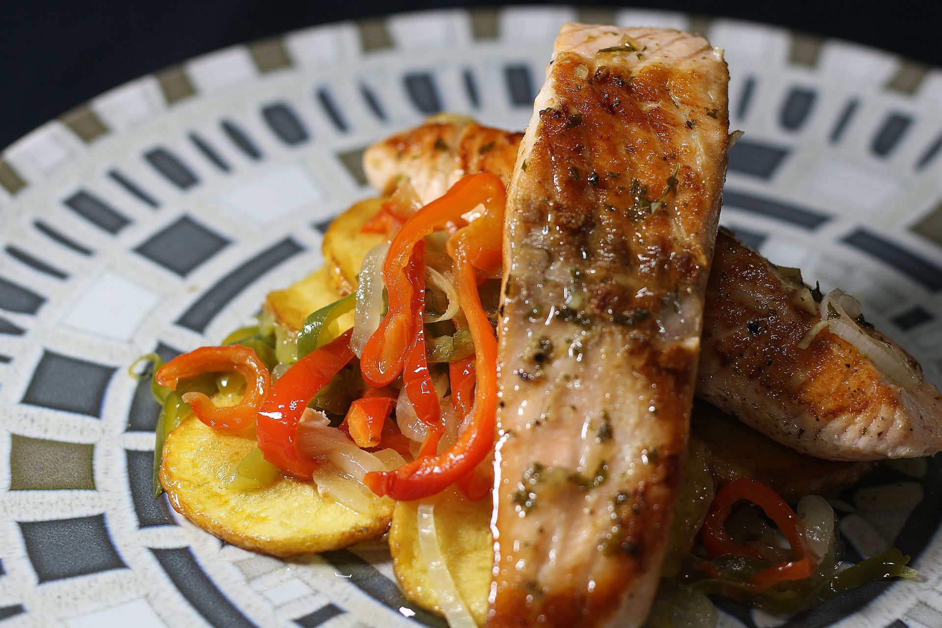Filete de salmón sobre rodajas de patata y pimientos salteados, servido en plato estampado.