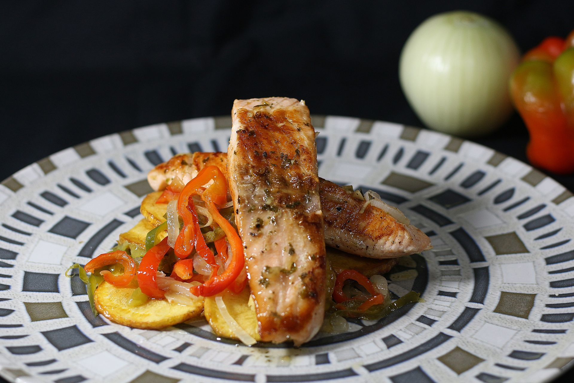 Filetes de salmón a la parrilla sobre patatas y pimientos salteados en un plato decorativo.