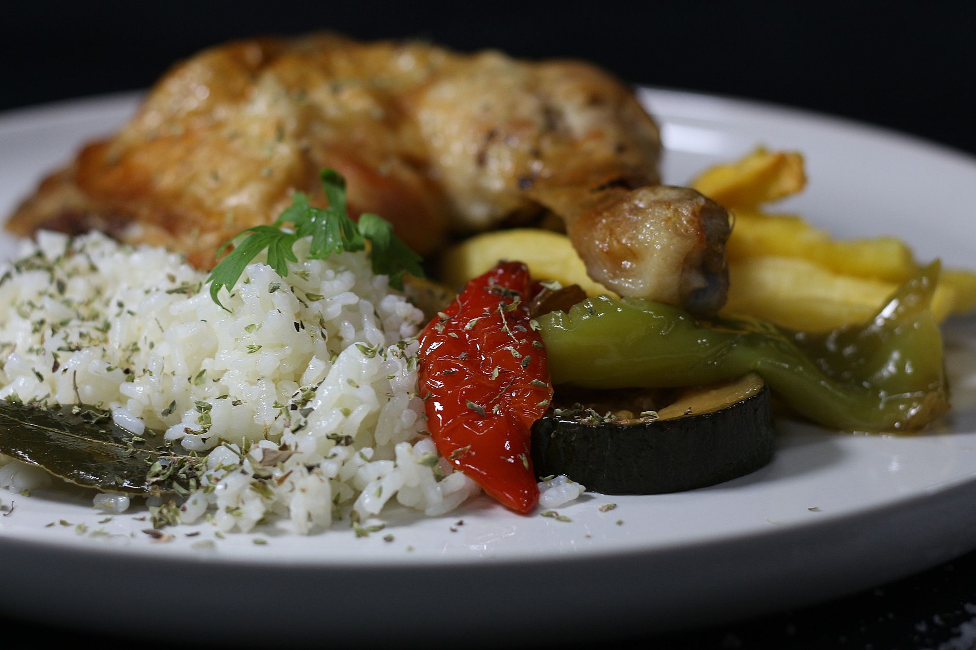 Pollo asado con arroz, verduras y hierbas en un plato blanco.