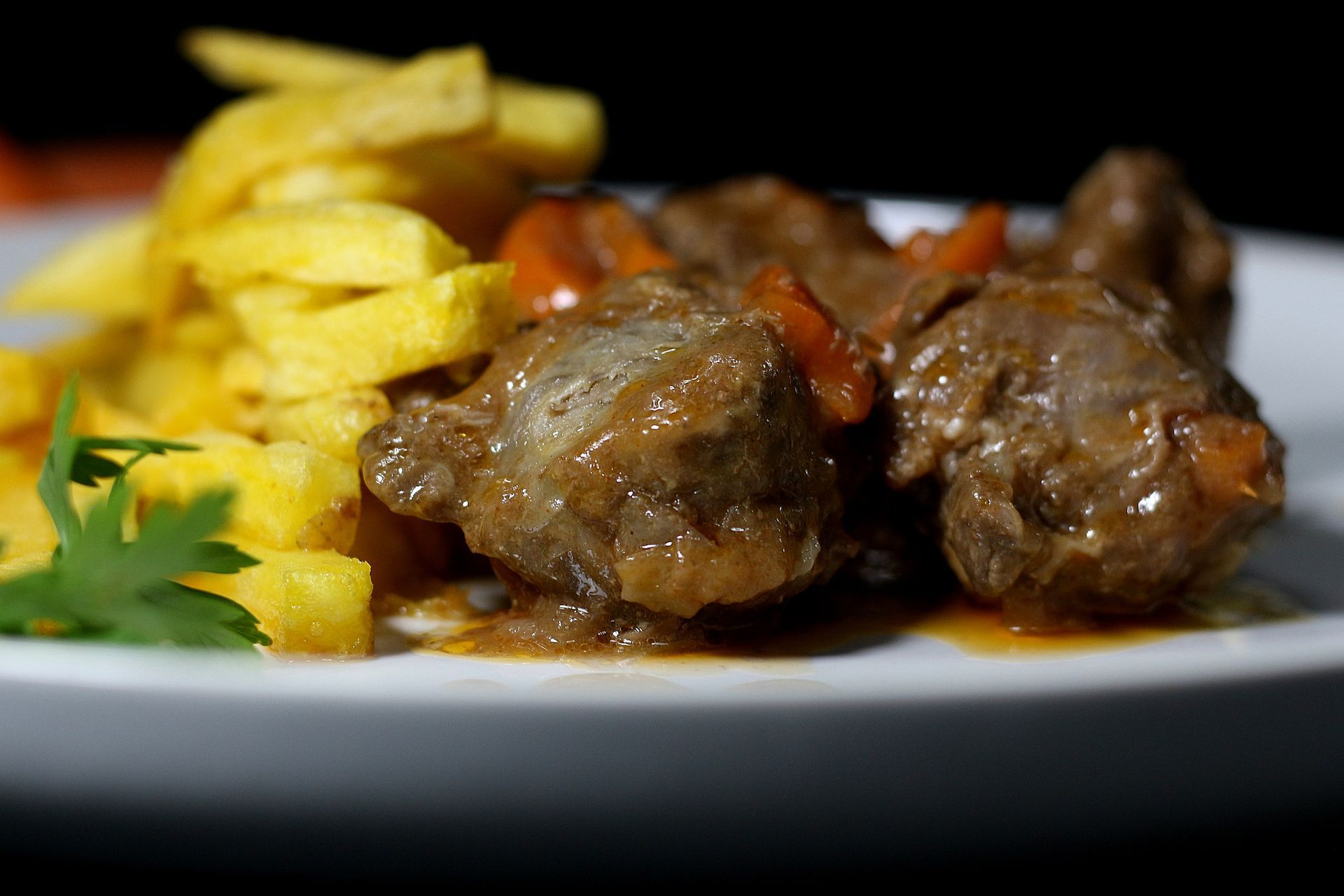 Carne guisada y zanahorias con patatas fritas en un plato blanco.
