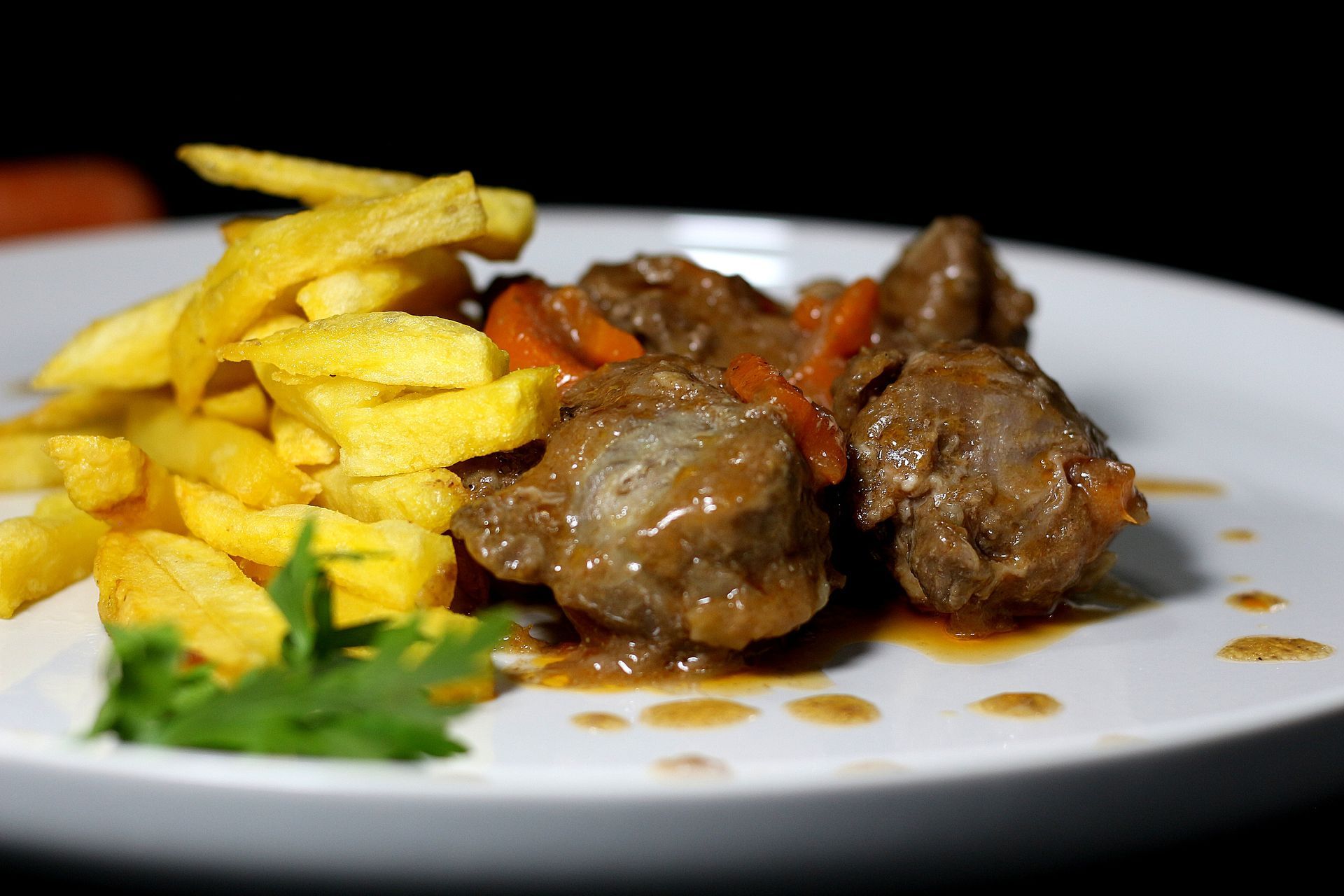 Carne guisada con zanahorias y patatas fritas en un plato blanco.