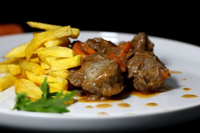 Carne guisada con zanahorias y patatas fritas en un plato blanco.