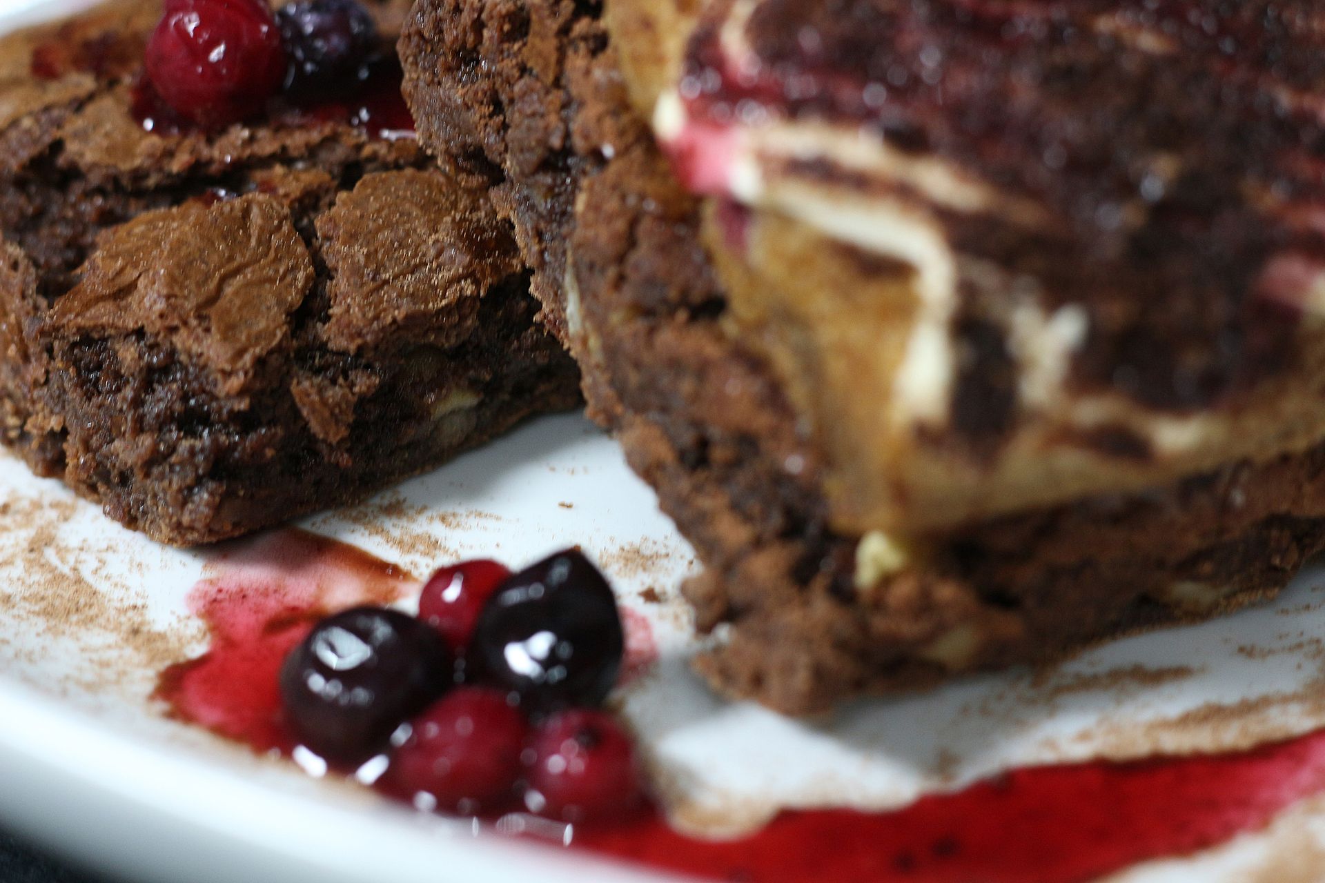 Rebanadas de brownie con cobertura de crema, bayas y salsa en un plato blanco.