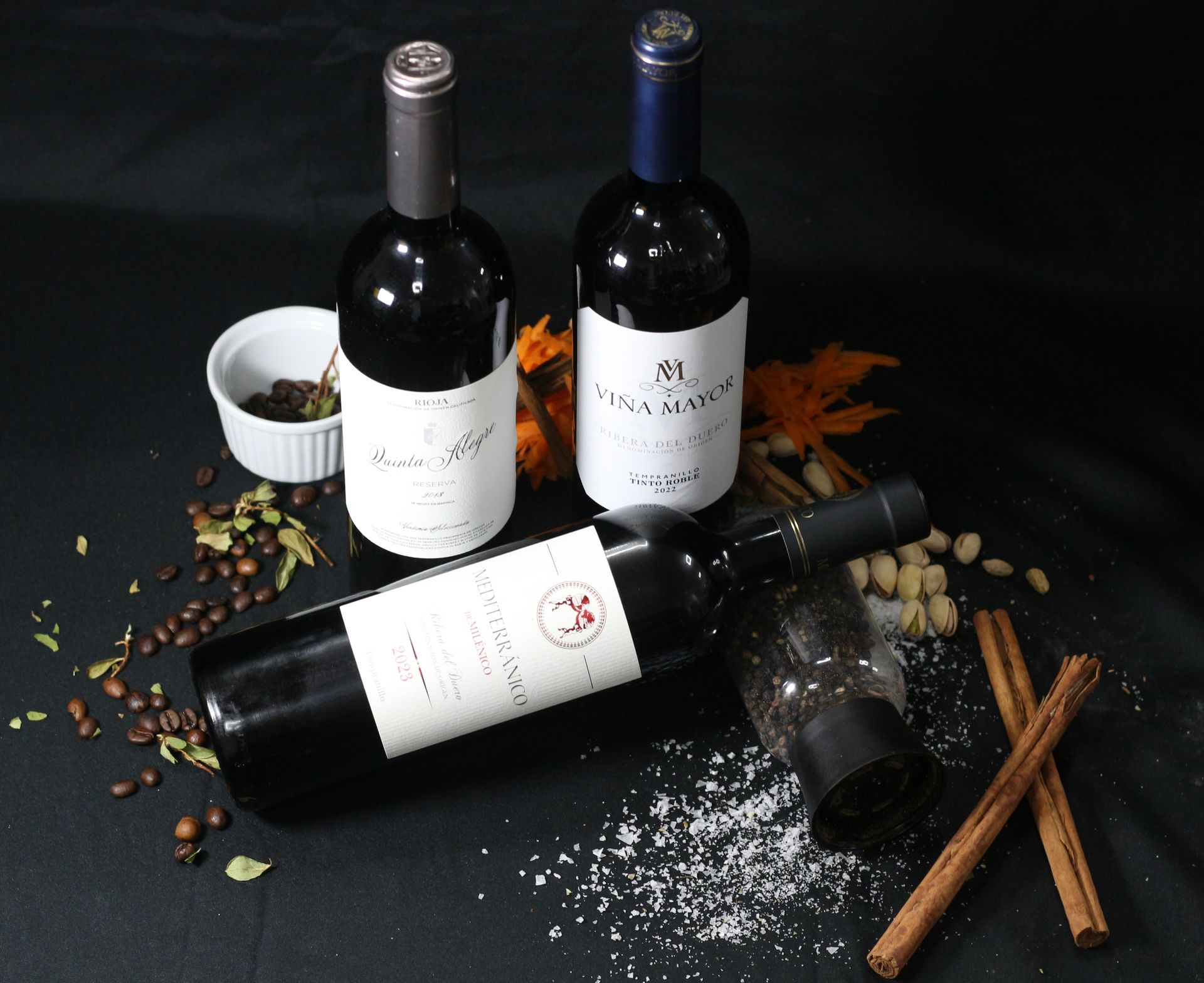 Tres botellas de vino tinto con especias sobre una superficie negra.