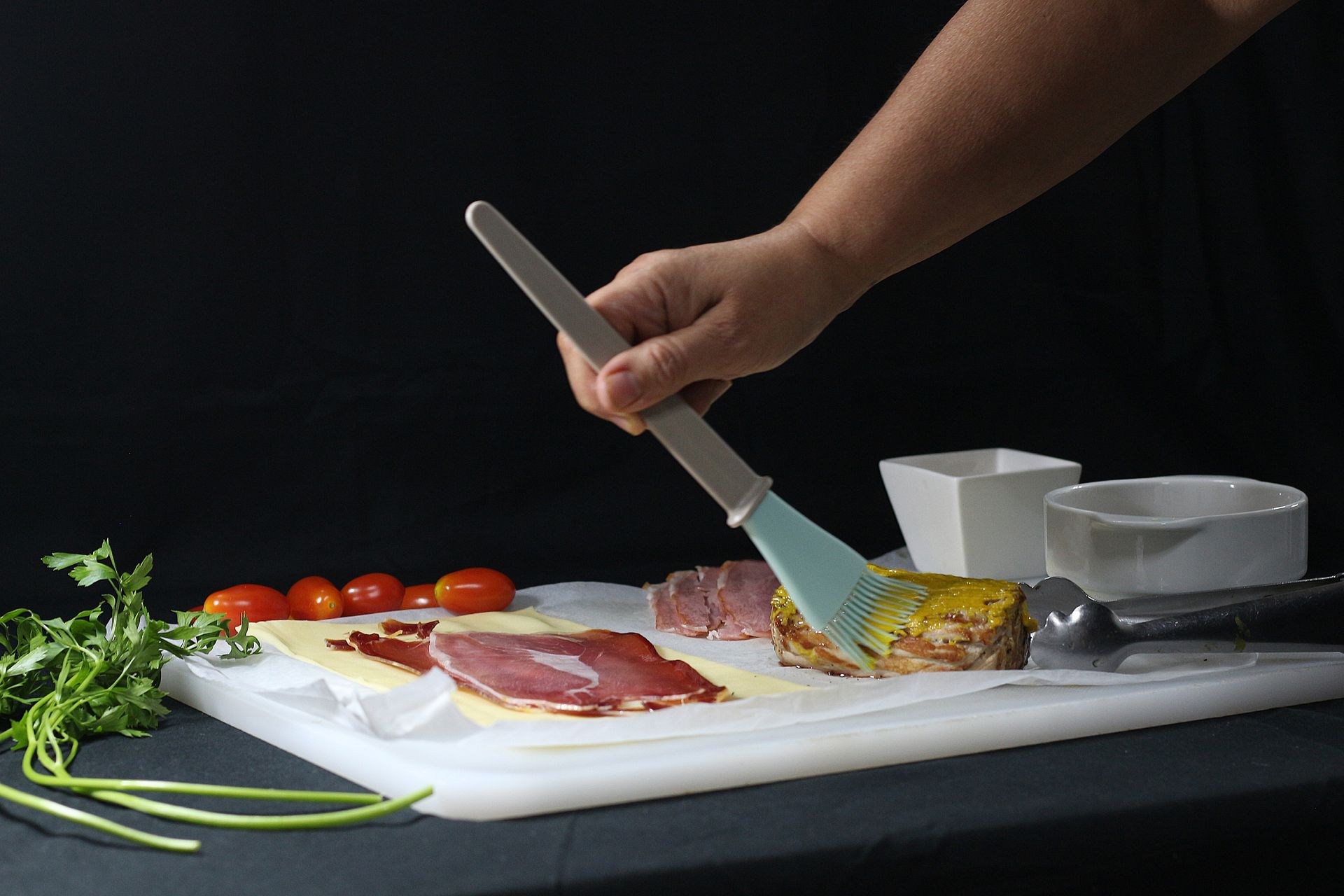 Pincelando a mano los alimentos sobre una tabla de cortar; los ingredientes incluyen carne, tomates y verduras.
