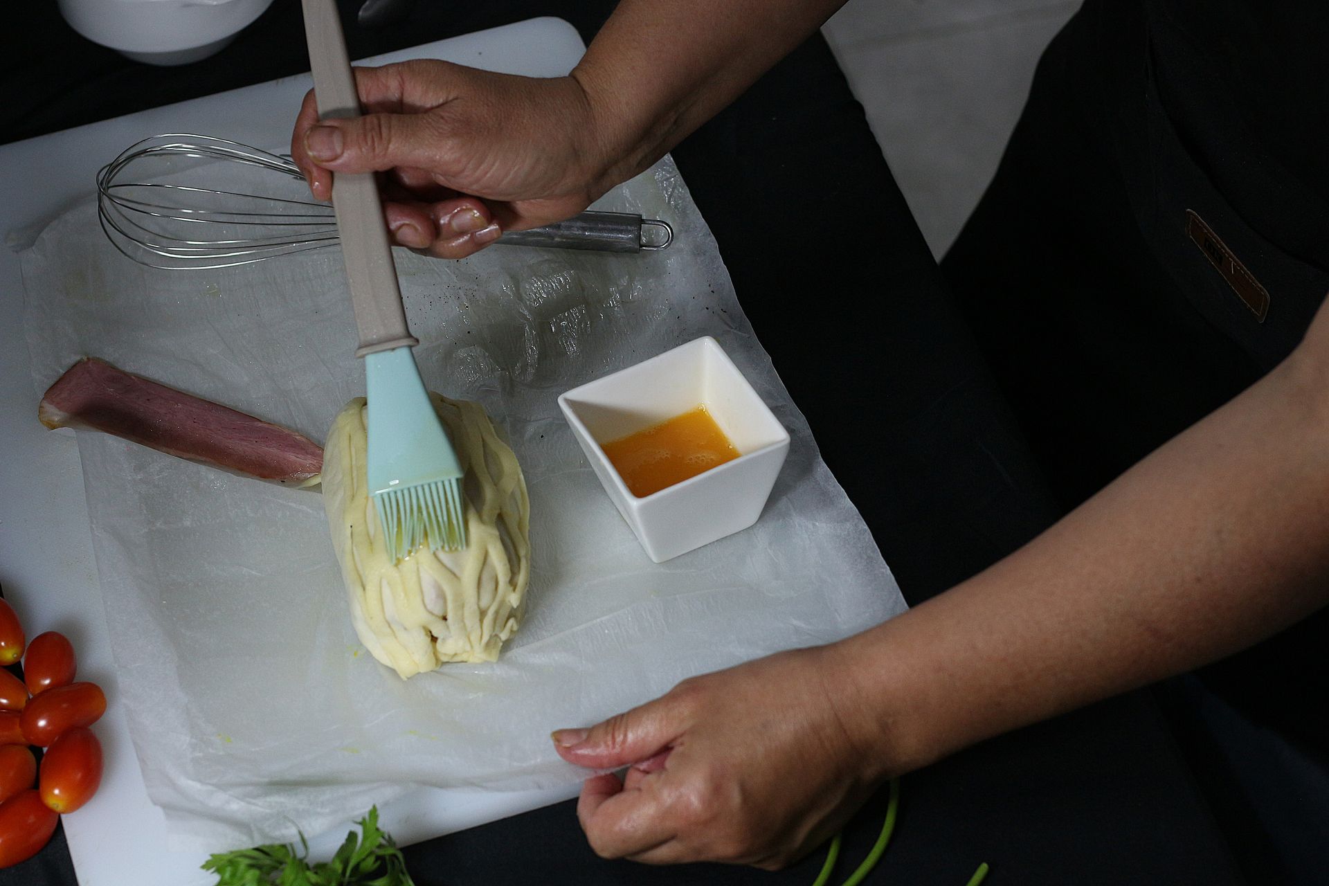 Una persona pincela con huevo batido la masa sobre una tabla de cortar.