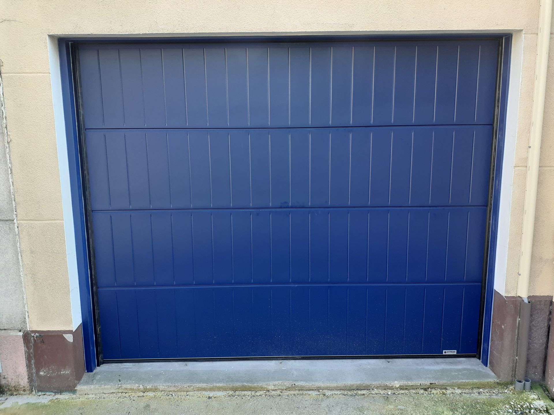 Porte de garage bleue fermée, encadrée de murs beiges et de plinthes brunes